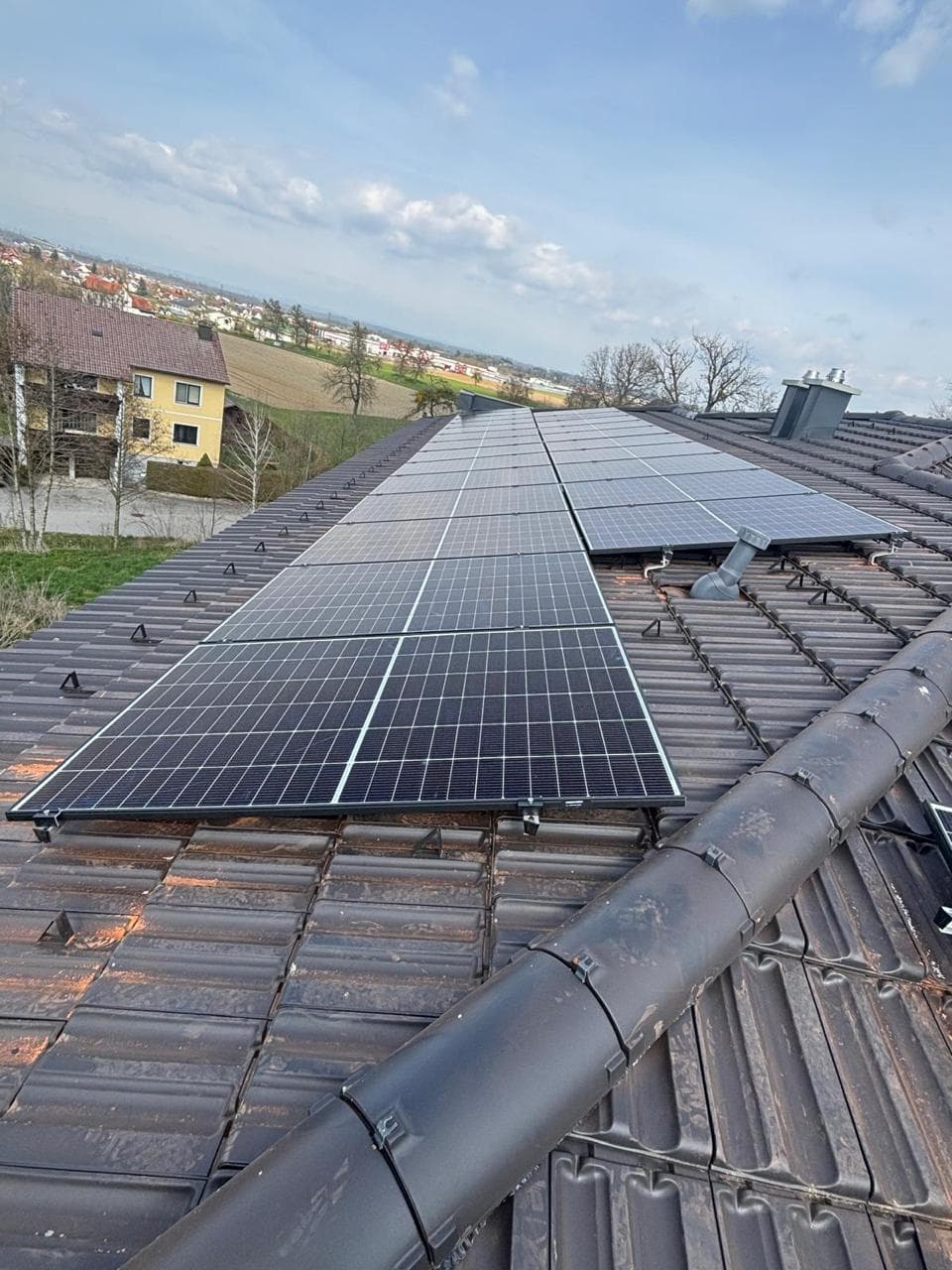 PV-Module auf dunklem Ziegeldach mit Dorfblick